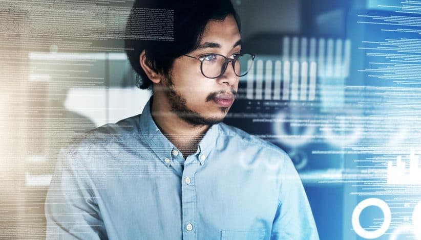 An engineer in glasses reading a dashboard reflected across the frame.